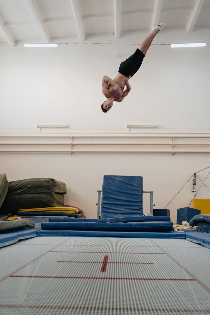 Athlete demonstrates incredible skill and agility while performing a flip on a trampoline indoors.